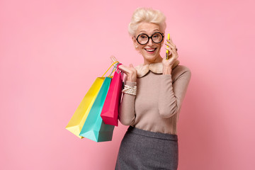 Beautiful happy woman holds shopping bags and talks by mobile phone. Photo of kind elderly woman on...