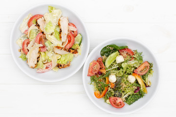 deep plates with fresh salad ingredients mixed with sauce placed on an attractive white table background. A place for a menu, banner or advertisement