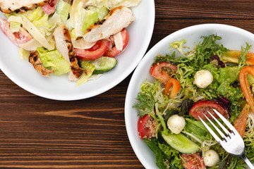 white deep plates with fresh salad ingredients mixed with sauce placed on an attractive background. A place for a menu, banner or advertisement
