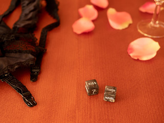 Playing sexual games with cubes. Cubes, suspenders, champagne glass and some pink rose petals on the table. Cubes with kiss and thigh label.