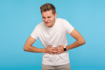Sick man grimacing from stomach ache, severe abdominal distress, feeling discomfort in belly,...