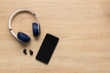 Stock photo of a bluetooth headphones and a smartphone on a wooden background and space for copy text