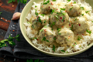 Hot Swedish meatballs with white rice and cranberry sauce on wooden table