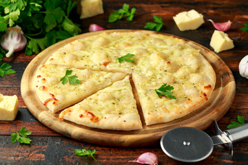 Garlic cheese pizza on wooden board with herbs.