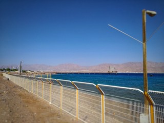 shiny fence. In the background is an empty beach and a turquoise ocean. White clouds on a blue sky