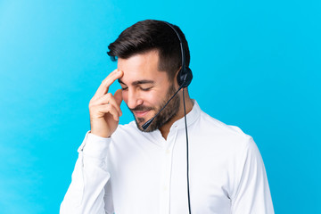 Telemarketer man working with a headset over isolated blue background laughing