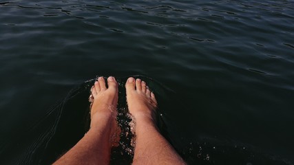 Naked hairy male legs hang from a catamaran. The legs of a man swim towards the waves on a ship. First person of view from the boat.