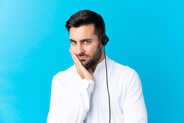 Telemarketer man working with a headset over isolated blue background unhappy and frustrated