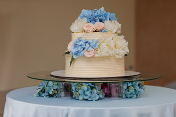 white wedding cake with blue hydrangeas and pink roses flowers on the table. Stylish flowers wedding day.