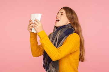 Allergy, flu sickness. Portrait of unhealthy red hair girl in big scarf, holding tissue and sneezing, blowing nose, suffering influenza, airborne disease epidemics. indoor studio shot pink background