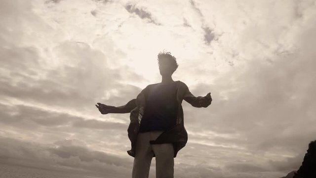 Madeira Island, Portugal - Man Meditating While Standing Under The Clouds With His Clothes Swaying In The Wind In Slow Motion - Low Angle Shot