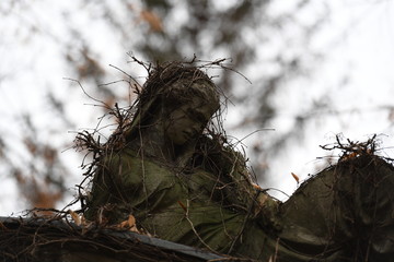 A resting, by leafless ivy overgrown angel in front of a blurred background.