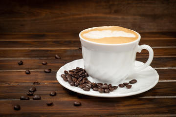 Cappuccino in a white glass on a saucer. Coffee beans on a saucer. Brown background