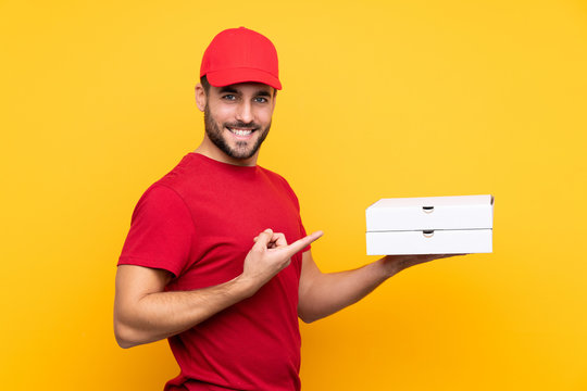 pizza delivery man with work uniform picking up pizza boxes over isolated yellow background and pointing it