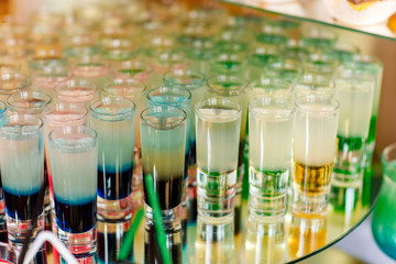 Many different colorful alcoholic shot cocktails in drinking glasses green brown red and white colors standing on mirror table on bar. set of alcohol mini cocktail shooters.