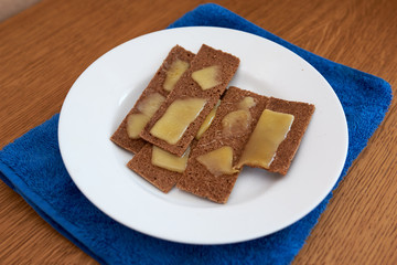 Dietary simple toasts dark bread crisps topped with melted cheese on a white round plate on a blue towel on a wooden table