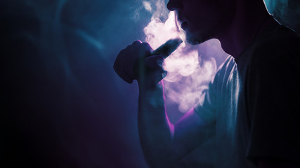 Close - up of a young man exhaling a cloud of steam or smoke using an electronic cigarette....