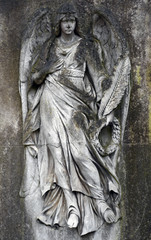 Fototapeta premium A weathered sandstone sculpture of an angel with a laurel wreath in her hand on a cemetery in Berlin-Germany.