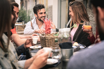 Multiracial friends, girls and guys, having fun laughing drinking coffee in coffeehouse, happy diverse young people talking joking sitting together at cafe, a couple watching each other into the eyes.