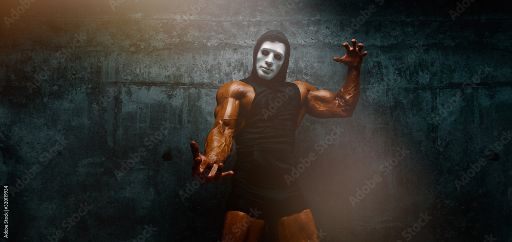 Wall mural mysterious muscular man hiding behind mask flexing muscles. bodybuilder with mask on his face posing - Wall murals