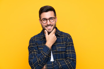 Fototapeta premium Young handsome man with beard over isolated yellow background with glasses and smiling