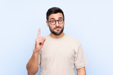 Young handsome man with beard over isolated blue background pointing with the index finger a great...