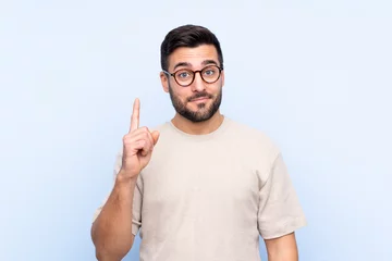 Foto op Plexiglas Young handsome man with beard over isolated blue background pointing with the index finger a great idea © luismolinero