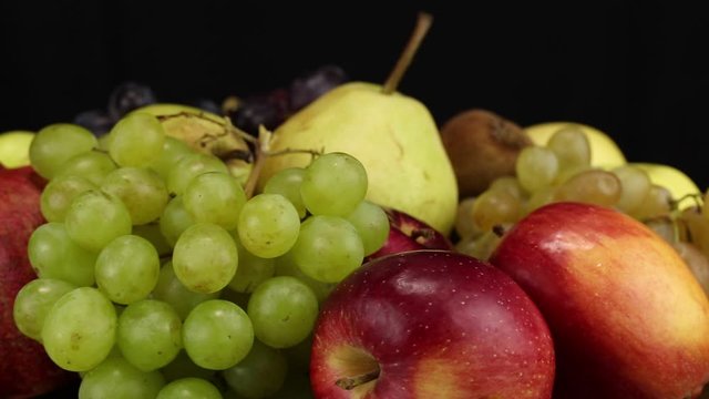 Red apples, green grapes and large pomegranate rotate counterclockwise, side view