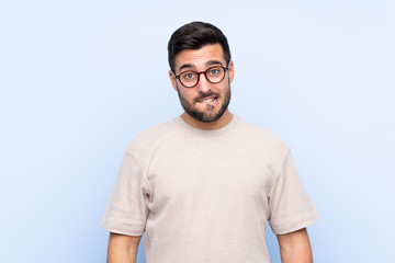 Young handsome man with beard over isolated blue background having doubts and with confuse face expression