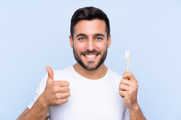 Young handsome man with beard brushing his teeth over isolated background with thumbs up because...