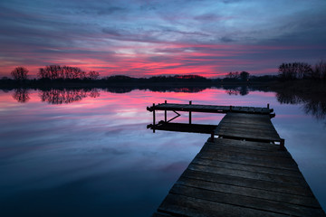 Pink sunset with dramatic clouds, lake and wooden jetty