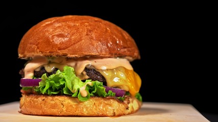 Craft burger is cooking on black background. Consist: sauce salsa, lettuce, red onion, pickle, cheese, chilli green pepper, bun, marbled meat beef.