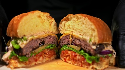 Cut craft burger is cooking on black background. Consist sauce salsa, lettuce, red onion, pickle, cheese, chilli green pepper, bun, marbled meat beef.