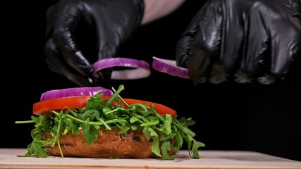 Craft burger is cooking on black background. Consist: sauce, arugula, tomato, onion, bacon, currant sauce, ricotta cheese, air bun and marble meat.