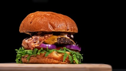 Craft burger is cooking on black background. Consist: sauce, arugula, tomato, onion, bacon, currant sauce, ricotta cheese, air bun and marble meat.