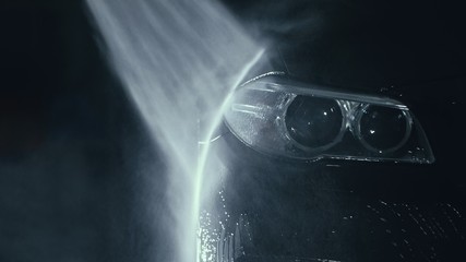 Car headlight wash. Washing modern vehicle body by high pressure jet wash hose water. Auto glass...