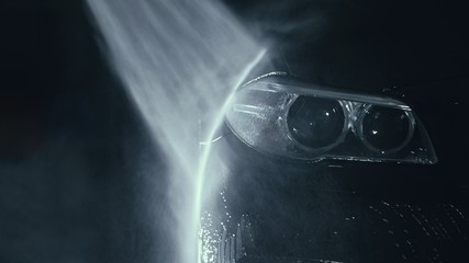 Car headlight wash. Washing modern vehicle body by high pressure jet wash hose water. Auto glass...