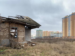 Old ruined house on the background of a new high-rise building. Abandoned house with no doors and windows with a broken roof. Concept: devastation, construction