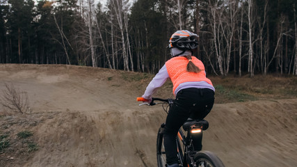 One caucasian children rides bike road track in dirt park. Girl riding black orange cycle in...