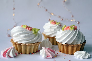 Cake with whipped cream and meringue. White, slightly grayish background. White green rose cream. Tartlet-shaped cake. Cake decorated with cream flowers 