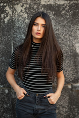 Beauty frontal portrait of a cheerful girl with green eyes and straight brown hair, dressed in casual clothes, makeup, supported by a black wall.