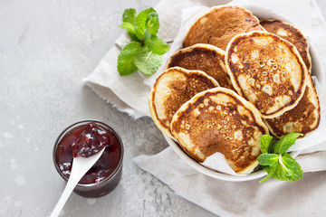 Pancakes with red berry jam and mint, light grey stone background. American cuisine. Breakfast. Top view.
