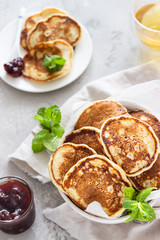 Pancakes with red berry jam and mint, light grey stone background. American cuisine. Breakfast. 