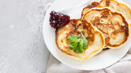 Pancakes with red berry jam and mint, light grey stone background. American cuisine. Breakfast. Top view.