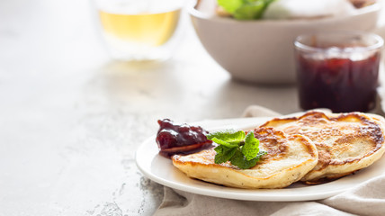 Pancakes with red berry jam and mint, light grey stone background. American cuisine. Breakfast. 