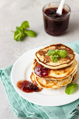 Pancakes with red berry jam and mint, light grey stone background. American cuisine. Breakfast. 