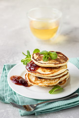 Pancakes with red berry jam and mint, herbal tea. American cuisine. Perfect idea for breakfast. Light grey stone background.