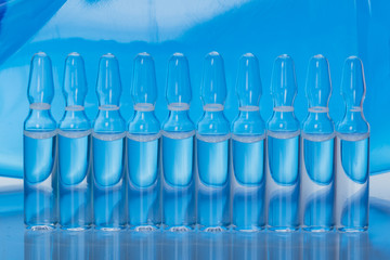 Glass medical ampoule vial for injection. Medicine is liquid sodium chloride with of aqueous solution in ampulla. Close up. Bottles ampule multicolor on background color and water. Human plasma.