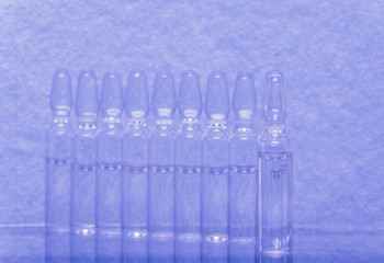 Glass medical ampoule vial for injection. Medicine is liquid sodium chloride with of aqueous solution in ampulla. Close up. Bottles ampule multicolor on background color and water. Human plasma.