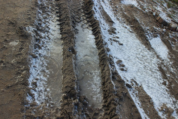 Bad road without asphalt, dirt, frost, ice crust on the ground, car tracks